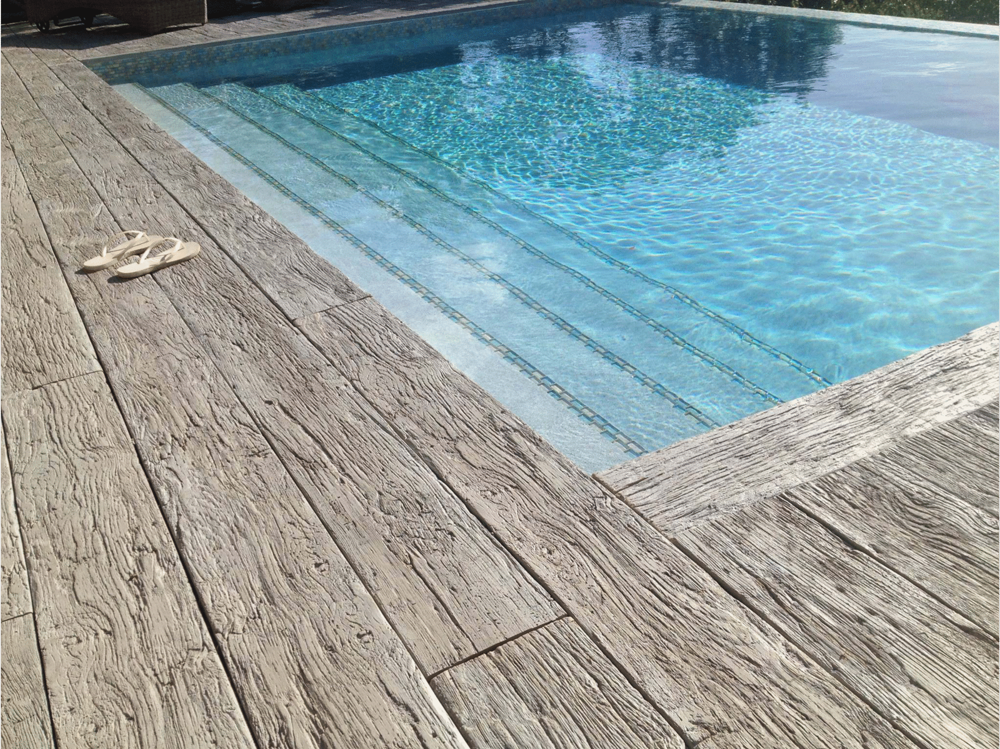 Weathered oak decking surrounds a pool with built-in steps; Millboard decking concept.