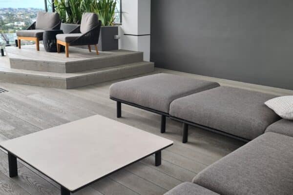 Building materials for homes, featuring a modern outdoor lounge area with grey furniture, wood-look flooring, and city views.