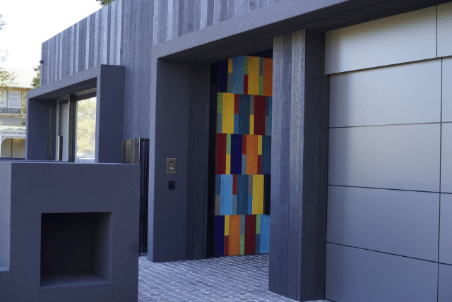 Building materials for homes, showcasing an exterior with grey wood siding, colourful tile accents, and a sleek, modern garage door.