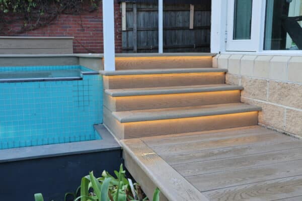 Luxury outdoor living: illuminated composite deck stairs leading to a modern home.
